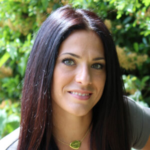 Woman with long dark hair in front of leafy trees.